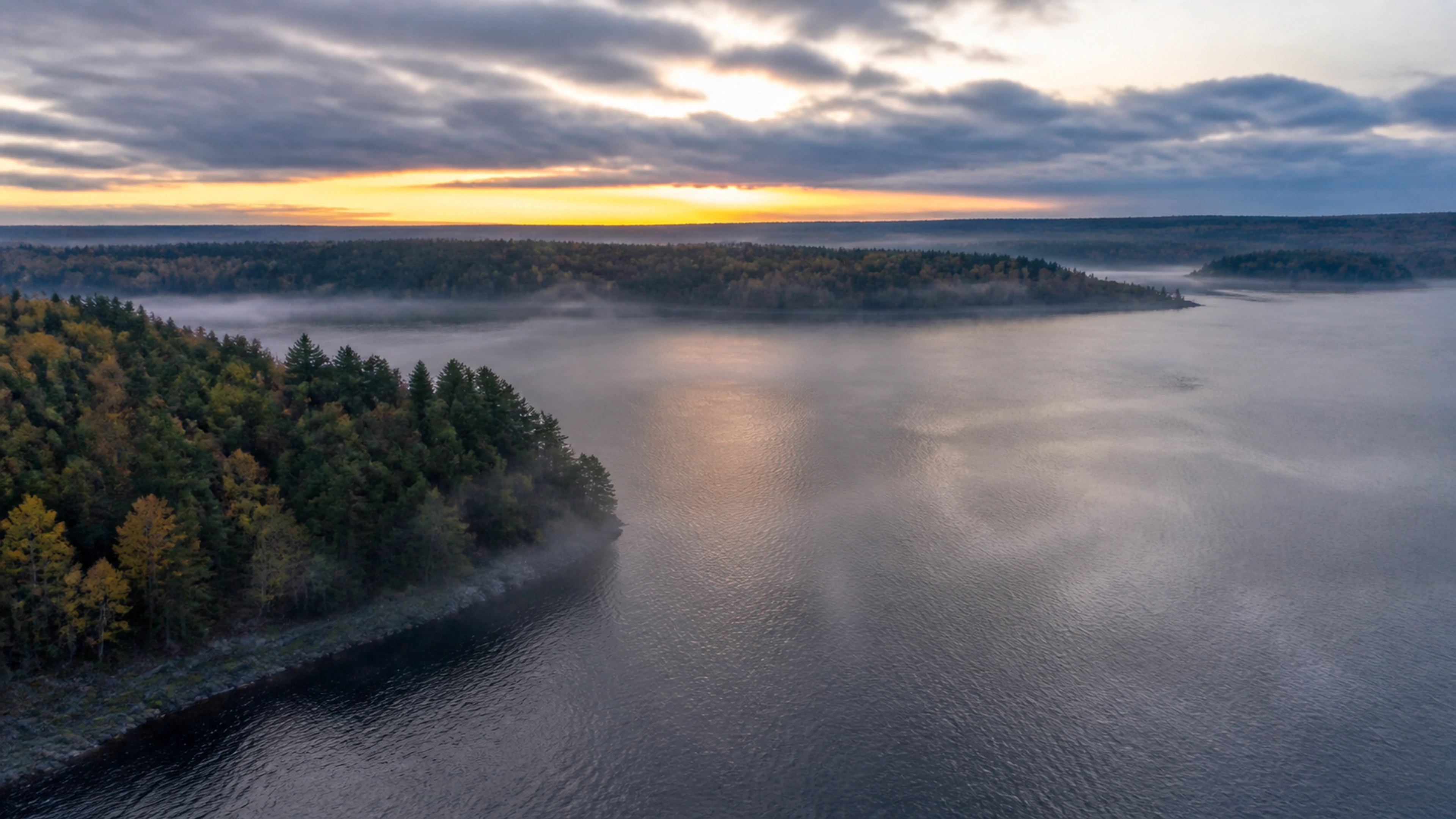 Mist lifting above a forest and lake at first light